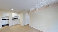 This 1-bedroom, 1-bathroom residence is thoughtfully laid out across a single floor, making efficient use of its space. The open living area features neutral-toned carpet flooring and light beige walls that create a clean, understated ambiance throughout. A textured ceiling adds subtle dimension to the space, while a ventilation unit overhead ensures comfortable climate control year-round. The kitchen is conveniently positioned adjacent to the living area, separated by a breakfast bar-style counter with dark countertops that provide a subtle contrast to the white cabinetry above and below. The kitchen is equipped with an under-cabinet range hood and offers ample storage through its white upper cabinets. A doorway from the main living area leads to the bedroom and bathroom, maintaining a straightforward and accessible flow between spaces. The overall design is simple and functional, with a neutral color palette throughout that provides a versatile backdrop for a variety of furnishing styles. The layout maximizes usability, making this a practical and comfortable living space well-suited for individuals or couples seeking a manageable, easy-to-maintain home.