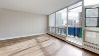 This 1-bedroom, 1-bathroom unit offers a thoughtfully designed layout across a single floor, combining functionality with a clean, modern aesthetic. Light-toned hardwood flooring runs throughout the unit, creating a bright and cohesive feel in every room. The spacious living room is a standout feature, anchored by expansive floor-to-ceiling windows that frame sweeping urban skyline views and allow abundant natural light to pour in. A private balcony is accessible directly from the living area, extending the living space outdoors. The kitchen is efficiently designed with white cabinetry, subway tile backsplash, stainless steel appliances including a refrigerator, stove, and built-in microwave, and a double sink with a modern faucet. The bedroom is a well-proportioned retreat featuring a double-door closet and its own large window overlooking the cityscape. The full bathroom is finished with neutral tile flooring, a white vanity, and a full-size soaking tub with shower. A dedicated entry foyer with a built-in closet adds practicality to the layout. Throughout the unit, neutral warm-grey walls complement the light flooring, contributing to a clean, contemporary ambiance well-suited to urban living.