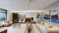 The lobby and common areas at 8035 Boulevard St-Laurent in Brossard, QC offer a thoughtfully designed communal environment spread across a generously sized single floor. The main lounge area serves as the heart of the space, featuring a modern fireplace with a bold yellow surround and decorative stacked logs, a tufted white Chesterfield sofa, and curated seating arrangements complemented by indoor plants and vibrant large-scale artwork. Floor-to-ceiling windows flood the lounge with natural light and provide open views of the surrounding streetscape, creating a bright, welcoming atmosphere with light tile flooring throughout.

The hallway connects all areas with a clean, contemporary aesthetic — warm wood-toned doors, textured wall finishes, and recessed skylights provide an inviting transition between spaces. A communal dining and lounge area features light hardwood flooring, patterned accent walls, and casual round tables with modern chairs, ideal for social gatherings. The kitchen is equipped with stainless steel appliances, ample white cabinetry, and a skylight overhead, offering a fully functional space for shared use. The exercise room is outfitted with free weights, an adjustable bench, floor-to-ceiling mirrors, and instructional fitness charts, providing residents with a practical and well-lit fitness facility.