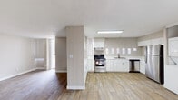 This single-floor unit offers a practical and comfortable layout designed for everyday living. The open-concept kitchen serves as the heart of the space, finished with crisp white shaker-style cabinetry extending from floor to ceiling, providing generous storage throughout. Light wood-look flooring runs across the kitchen and common areas, creating a clean and cohesive look. The kitchen is well-equipped with stainless steel appliances, including an electric range with overhead ventilation, a dishwasher, and a full-size refrigerator. A double-basin sink is positioned beneath a row of small windows that allow natural light to filter in. Ample counter space lines the walls, making the kitchen highly functional. Conveniently tucked within the kitchen area is a stacked washer and dryer unit, offering in-unit laundry without sacrificing significant space. A structural column subtly defines the transition between the kitchen and the adjacent living area, which continues the wood-look flooring. The bedroom features wall-to-wall carpet in a warm neutral tone, offering a cozy and quiet retreat. The textured ceilings are consistent throughout the unit. The bathroom is finished with white tile, a tub-shower combination, a large vanity mirror with overhead lighting, and a clean, straightforward design. Overall, the unit presents a neutral palette that is both versatile and move-in ready.