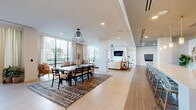 Located at 615 E Morehead Street in Charlotte's vibrant Midtown district, this generously sized single-floor amenity lounge offers a thoughtfully designed open-plan layout that seamlessly blends comfort, functionality, and modern style. The space is anchored by large floor-to-ceiling windows that flood the interior with natural light while framing striking views of the Charlotte skyline and adjacent outdoor terrace.

The main gathering area features a spacious lounge with plush neutral seating, a sleek wall-mounted television, and built-in shelving — ideal for both relaxed socializing and group events. Adjacent to the lounge, a formal dining area accommodates a large table beneath an elegant pendant light fixture, complemented by rich area rugs and neutral drapery that soften the contemporary aesthetic.

A well-appointed wet bar serves as a central hub, featuring a white tile backsplash, dark cabinetry with gold hardware, open floating shelves, and a row of stylish woven bar stools beneath warm pendant lighting. A secondary kitchenette area provides additional counter space and storage with refined finishes.

The game zone features a billiard table and wall-mounted game board, while an entry corridor with wood-look tile flooring and built-in shelving provides a clean, welcoming transition into the space. Throughout, recessed lighting, structural columns, and a neutral palette create a cohesive, upscale ambiance.