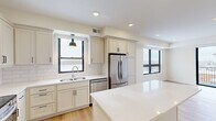 This thoughtfully designed one-bedroom, one-bathroom unit offers a cohesive modern aesthetic throughout its efficiently utilized single floor. Light hardwood flooring flows through the main living areas, complemented by warm neutral wall tones and black-accented hardware and window frames that add a contemporary edge.

The kitchen is a standout feature, outfitted with cream shaker-style cabinetry extending to the ceiling, a white subway tile backsplash, quartz countertops, and a full suite of stainless steel appliances including a refrigerator, range, microwave, and dishwasher. A central island provides additional prep and dining space, while a pendant light and large window enhance the bright, functional atmosphere.

The living room opens to a private balcony through floor-to-ceiling sliding glass doors, offering outdoor views and ample natural light. The bedroom features plush carpeting, a large window with exterior views, and a built-in closet. The bathroom is finished with a white vanity, quartz countertop, wood-look tile flooring, and a glass-enclosed shower adorned with marble-style tile. A dedicated in-unit laundry room houses a full-size washer and dryer with overhead shelving for added storage convenience.