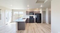 Located at 2750 George Elmer Dr in Missoula, Montana, this efficiently designed single-floor unit offers a thoughtful layout that maximizes every square foot. Light wood-tone vinyl plank flooring runs throughout, giving the space a clean, cohesive aesthetic.

The open-concept living area is bright and airy, anchored by a wall-mounted HVAC unit and a window that frames picturesque mountain views — a standout feature that brings the natural beauty of Montana indoors. A private entry door provides direct access to an outdoor balcony area.

The kitchen is well-appointed, featuring dark-toned cabinetry, black appliances including a range with overhead microwave and a full-size refrigerator, and light-colored countertops. A peninsula with a built-in sink adds functional prep space and serves as a natural divider between the kitchen and living areas. Recessed lighting illuminates the kitchen, adding to the modern, practical feel.

The full bathroom includes a soaking tub, a toilet, a dark-cabinetry vanity with a stone-look countertop, and matte black fixtures and hardware for a contemporary touch. Light wood flooring continues into the bathroom, maintaining visual consistency.

Additional practical features include an electrical panel, recessed lighting, and a smoke detector. The overall palette of neutral warm tones creates a welcoming, move-in-ready environment.
