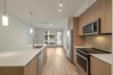 Located at 6161 Fairmount Ave, Unit 280 in San Diego, CA, this thoughtfully designed single-floor residence offers a clean, contemporary aesthetic throughout. The open-concept kitchen serves as the heart of the unit, showcasing flat-front wood-toned cabinetry that extends to the ceiling, a suite of stainless steel appliances including a french door refrigerator, electric range, and built-in microwave, complemented by a light-colored tile backsplash. A generously sized center island with a crisp white countertop and an integrated sink with a modern pull-down faucet anchors the space, illuminated by stylish pendant lighting and a track lighting system overhead. Light wood-style flooring runs throughout the main living areas, creating a warm yet contemporary feel, while large windows and a glass sliding door invite abundant natural light and provide outdoor views. The bedrooms are finished with plush carpet and feature well-sized windows with views of the surrounding greenery. The bathrooms are elegantly appointed with large-format white marble-look tile covering both the floors and tub surrounds, paired with brushed nickel fixtures for a polished finish. A smart thermostat and in-unit laundry further enhance the functionality of this modern San Diego residence.