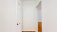 Located at 432 S New Hampshire Ave in the heart of Los Angeles, CA, this single-floor unit offers a well-organized layout that maximizes every square foot. The open-concept main area seamlessly combines the living room, dining space, and kitchen, creating a cohesive and functional environment. Warm parquet wood flooring extends throughout the living and dining areas, lending a classic character to the bright, white-walled interior. A ceiling fan anchors the living space, while a large picture window invites natural light and outdoor views. A built-in shelving unit with an integrated desk provides a practical workspace and display area, adding architectural interest to the main living zone. The kitchen is outfitted with white cabinetry, a gas range, full-size refrigerator, and a built-in range hood, with tile flooring that transitions cleanly from the parquet. A breakfast bar with seating connects the kitchen to the living area. The dining nook benefits from a window overlooking the street, keeping the space light-filled. The bathroom features a pedestal sink, toilet, a shower-tub combination, and tile flooring, all finished in a clean, minimalist white palette. Two hallways provide efficient circulation throughout the unit, contributing to a well-connected and easy-to-navigate floor plan.