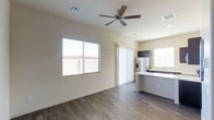 This single-floor residence offers a clean, modern aesthetic defined by an open-concept layout that seamlessly connects the living area to the kitchen. The living space features warm wood-style laminate flooring, neutral wall tones, and a ceiling fan overhead, contributing to a comfortable and airy atmosphere. Large windows along the exterior walls invite generous amounts of natural light throughout the day, while a sliding glass door provides access to an outdoor area, further enhancing the sense of openness.

The kitchen is thoughtfully designed with dark cabinetry contrasted against a light countertop surface, offering a contemporary look. A stainless steel refrigerator with an in-door dispenser anchors the space, which also includes a sink positioned beneath a bright window. The kitchen island or peninsula provides additional workspace and serves as a natural transition point between the culinary and living areas.

Recessed lighting and ceiling-mounted vents are integrated into the layout, ensuring both functional comfort and a streamlined visual appearance. The overall design prioritizes a bright, neutral palette that lends versatility to the space, making it well-suited for a variety of interior styles. The combination of modern finishes and practical layout makes this a highly functional and welcoming single-floor living environment.