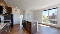This single-floor residence offers a well-designed open-concept layout that seamlessly connects the kitchen and living areas. The kitchen serves as the centerpiece of the main living space, anchored by a substantial island topped with light granite countertops that also extends to the perimeter counters. Dark espresso-toned cabinetry provides generous storage and contrasts cleanly against the white walls, while a full suite of stainless steel appliances — including a refrigerator, range, microwave, and dishwasher — adds a polished, contemporary finish. Wood-style flooring runs throughout the main living areas, contributing warmth and continuity to the open floor plan.

Multiple windows allow abundant natural light to fill the living space, offering views of the surrounding exterior. The bedroom features plush carpeting and a large picture window that frames outdoor views and draws in significant daylight, creating a bright and airy atmosphere.

The bathroom is clean and functional, appointed with a dark-vanity cabinet, white countertop, and a full tub-shower combination with brushed nickel fixtures. The overall design aesthetic throughout the unit is modern and neutral, with a consistent use of white walls, warm wood tones, and contemporary finishes.