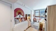 Located at 299 Duffield St in Downtown Brooklyn, this efficiently designed single-bedroom unit offers a well-organized layout across one floor. The main living and sleeping area is bright and airy, thanks to large, floor-to-ceiling windows with warm wood frames that flood the space with natural light and offer open views of the surrounding Brooklyn streetscape. The hardwood flooring throughout adds warmth and continuity to the compact interior.

The bedroom is thoughtfully arranged to maximize functionality, featuring a built-in desk with integrated shelving and under-cabinet lighting — ideal as a dedicated workspace. A closet provides additional storage within the unit. The crisp white walls create a clean, neutral backdrop that enhances the sense of openness.

The bathroom is neatly appointed with a wood-accented vanity, a large wall mirror, and tile flooring, maintaining the modern and tidy aesthetic carried throughout the rest of the unit. A colorful striped bath mat adds a subtle decorative touch.

Overall, the unit presents a smartly efficient use of space, with purposeful built-ins, ample natural light, and contemporary finishes that make it a practical and inviting living environment in one of Brooklyn's most well-connected neighborhoods.