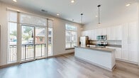 Located at 41 N Rangeline Rd, this thoughtfully designed one-bedroom, one-bathroom unit offers a contemporary living experience with clean lines and modern finishes throughout. The open-concept layout maximizes the efficient use of space, creating a bright and airy atmosphere enhanced by soaring ceilings and generous natural light from multiple windows fitted with classic horizontal blinds.

The kitchen serves as a standout feature, anchored by a large center island with a quartz-style countertop, undermount sink, and pendant lighting overhead. White shaker cabinetry extends to the ceiling, complemented by a full suite of stainless steel appliances including a refrigerator, range, and microwave. Light wood-look flooring ties the kitchen and living areas together seamlessly. In-unit washer and dryer hookups add everyday convenience.

The bedroom is a comfortable retreat, offering plush carpeting, soaring walls, and a large window that invites natural light and outdoor views. The space connects directly to a well-appointed closet and a sleek full bathroom featuring a double-sink vanity with white cabinetry, quartz countertops, matte black fixtures, and a glass-enclosed walk-in shower. The overall palette of whites, warm neutrals, and dark trim accents creates a cohesive, modern aesthetic throughout the entire unit.