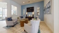 Located at 1301 Charter Colony Pkwy in Midlothian, Virginia, this thoughtfully designed single-floor amenity space offers a welcoming and upscale environment for gathering and socializing. The open-concept layout flows seamlessly between several distinct functional areas, all unified by elegant marble-look tile flooring that extends throughout.

The centerpiece of the space is a well-appointed kitchen featuring a large island with a bold blue countertop and seating for multiple guests, sleek taupe cabinetry, stainless steel appliances, and a striking slatted ceiling detail with pendant lighting overhead. The kitchen opens directly into a spacious communal dining area lined with upholstered chairs, teal drapery, and ample natural light streaming through large windows.

Adjacent to the dining area, a bright and airy seating nook features a round marble-top table surrounded by teal velvet accent chairs with nailhead trim, positioned beside French doors that open to an outdoor terrace with views of the surrounding community.

A cozy lounge area anchors another corner of the space, highlighted by a dusty blue accent wall, a wall-mounted television, and an arrangement of plush gray upholstered seating centered around warm wood accent tables. Curated artwork and decorative accents throughout lend a polished, cohesive aesthetic to the entire space.
