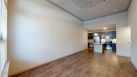 This single-floor residence showcases a thoughtfully designed open-concept layout that seamlessly connects the living area and kitchen. The living space immediately impresses with its dramatically high ceilings and rich hardwood-style flooring, creating an expansive, airy atmosphere. Large windows allow generous natural light to fill the room, offering views of the surrounding exterior.

The kitchen is a standout feature, outfitted with dark espresso cabinetry that extends to the ceiling, light granite countertops, a tile backsplash, and a full suite of stainless steel appliances including a French door refrigerator with ice maker, electric range, microwave, and dishwasher. A center island provides additional counter space and serves as a natural gathering point, while pendant lighting above adds a polished finishing touch.

The bedroom offers a comfortable, carpeted retreat with a large window that brings in ample natural light. The bathroom is finished with matching granite countertops, a dark-framed vanity mirror, tile-surround soaking tub, and hardwood-style flooring, maintaining the cohesive design language found throughout the home.

Overall, the space presents a contemporary aesthetic with high-quality finishes, generous proportions, and a well-considered floor plan suited for both everyday living and entertaining.