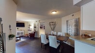 This single-floor residence offers a thoughtfully designed layout with a warm, inviting ambiance throughout. The open-concept living and dining area serves as the heart of the home, featuring rich dark hardwood-style flooring, a textured ceiling, and a ceiling fan overhead. The living room opens directly to an outdoor balcony through sliding glass doors with vertical blinds, allowing natural light to fill the space. The adjacent dining area accommodates a substantial wooden dining table with white upholstered chairs, complemented by decorative wall art.

The kitchen is well-equipped with white cabinetry, dark appliances including a refrigerator, dishwasher, and built-in cooktop, along with a peninsula that provides additional prep space and a pass-through view to the dining area. A window above the sink brings in natural light.

The primary bedroom is a comfortable retreat featuring a ceiling fan, a window with blinds, and access to an outdoor balcony. Its en-suite bathroom includes a single vanity with a wide mirror and overhead lighting. A secondary bedroom offers carpeted flooring and a walk-in closet with built-in shelving. A second full bathroom features a tub-shower combination with tiled surround, a single vanity, and a window for natural ventilation.