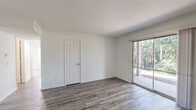 This single-story, 2-bedroom, 1-bathroom residence is designed for comfortable everyday living, featuring a clean, neutral palette and a well-organized layout throughout. The living room is bright and open, with durable wood-style plank flooring, white walls, and a textured ceiling. A sliding glass door connects the space directly to the patio, offering views of mature trees and bringing in generous natural light.

The combined kitchen and dining area is functional and well-equipped, featuring dark espresso-toned shaker cabinetry, light countertops, and black appliances including a full-size refrigerator, range, and dishwasher. Light wood-style flooring continues throughout this area, and recessed lighting keeps the space well-lit.

Both bedrooms are carpeted for comfort, with bright white walls and ample natural light through slatted-blind windows. The primary bedroom includes a closet, and additional closets throughout the unit — four in total — provide excellent storage options. The hallways connect the rooms efficiently within the compact single-floor plan.

The bathroom features classic white subway tile wainscoting, a white vanity with a single sink, brushed nickel fixtures, a wall-mounted mirror, and a louvered closet door, giving it a clean and timeless look. The patio offers an outdoor extension of the living space with pleasant wooded surroundings.