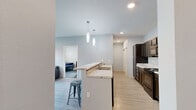 This single-floor, 3-bedroom, 3-bathroom unit offers a thoughtfully designed layout that balances communal and private living. The open-concept kitchen and living area serves as the heart of the home, featuring light wood-look flooring, soft gray walls, and recessed lighting complemented by stylish pendant fixtures. The kitchen is equipped with dark espresso cabinetry, granite-style countertops, and black appliances including a range, microwave, and refrigerator. A peninsula with bar seating provides additional dining and gathering space, seamlessly connecting the kitchen to the living area, which offers a window for natural light. Each of the three bedrooms is carpeted and includes a closet, providing personal storage for each occupant. The bathrooms are consistently finished with dark vanity cabinetry, granite-style countertops, and light tile flooring. Two bathrooms feature a shower/tub combination, while a third includes a walk-in shower. Additional spaces include a dedicated laundry room, a utility room, four closets, two hallways, and an entrance foyer — providing excellent functionality throughout. The unit's efficient and cohesive design makes it well-suited for shared occupancy.