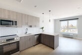 Unit 507 at 1213–1221 Broad St is a thoughtfully designed one-bedroom, one-bathroom residence that blends contemporary finishes with a clean, modern aesthetic throughout its single-floor layout. Light hardwood flooring flows seamlessly across the open living area and into the bedroom, lending warmth and continuity to the space.

The kitchen is a standout feature, showcasing sleek, textured gray cabinetry extending from floor to ceiling, a white subway tile backsplash, light quartz countertops, and a full suite of stainless steel appliances including a refrigerator, range, microwave, and dishwasher. A peninsula with pendant lighting above creates a natural divide between the kitchen and living area while offering additional prep and seating space.

The bedroom is a comfortable, well-proportioned room filled with natural light from a large window overlooking the surrounding cityscape. A double-door closet provides generous storage, and the room's neutral palette keeps the atmosphere calm and versatile.

The bathroom features light tile flooring, a dark vanity, and matte black grab bars and hardware accents, combining accessibility with a refined, modern look. Clean white walls and minimalist fixtures complete the space. Overall, Unit 507 presents a polished, move-in-ready residence with contemporary design details throughout.