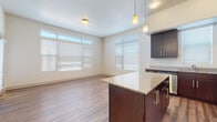 This single-floor residence offers a well-designed layout with a clear separation between living, kitchen, and sleeping areas. The kitchen serves as a central highlight, showcasing rich dark-espresso cabinetry paired with granite countertops, a central island with pendant lighting above, and a full suite of stainless steel appliances including a refrigerator, range, microwave, and dishwasher. Wood-look plank flooring runs throughout the kitchen and adjoining living area, adding warmth and continuity to the space.

The open living area benefits from an abundance of natural light, courtesy of large windows fitted with horizontal blinds. A transom window above the main window bank further enhances the brightness of the room, creating an airy and welcoming atmosphere.

Multiple bedrooms are finished with plush wall-to-wall carpeting and individual windows that allow natural light to filter in. Each room offers a clean, neutral palette well-suited for a variety of furnishing styles.

The two bathrooms are finished consistently, featuring granite-topped dark vanities, tile flooring in a natural stone pattern, and a tub-shower combination with chrome fixtures, providing a cohesive and functional design throughout.