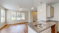 This well-appointed single-story home in Auburn, Alabama offers three bedrooms and three bathrooms across a thoughtfully designed floor plan. The open-concept living area is anchored by a bright living room with a ceiling fan and large windows that invite abundant natural light and outdoor views. The kitchen is a standout feature, showcasing granite countertops, a peninsula with a built-in sink and breakfast bar overhang, stainless steel appliances including a refrigerator, range, and microwave, and raised-panel cabinetry. Pendant lighting above the peninsula adds a polished finishing touch. Hardwood-style flooring flows throughout the main living, kitchen, dining, and hallway areas, while the bedrooms are finished with plush carpet and ceiling fans. Each bedroom offers natural light through slatted blinds. The bathrooms mirror the kitchen's quality finishes, featuring granite-topped vanities with raised-panel cabinetry and wood-look tile flooring. One bathroom includes a soaking tub and shower combination. A dedicated laundry room and five closets provide ample storage. The central hallway connects all rooms efficiently, and the home's neutral palette creates a clean, cohesive aesthetic throughout.