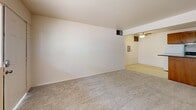 Located at 5201 East 2nd Street in Tucson, Arizona, this one-bedroom, one-bathroom unit offers a practical and efficient single-floor layout. The open living area features neutral carpet flooring and painted brick walls, creating a clean, understated backdrop. A ceiling fan overhead provides airflow and lighting, while the space flows directly into the kitchen area, which is set apart by tile flooring. The kitchen is equipped with warm-toned wood cabinetry — both upper and lower — along with a white refrigerator, electric range, and a double sink with a dark countertop. A recessed light illuminates the workspace, and a peninsula-style counter adds a subtle division between kitchen and living areas. The bedroom is a comfortable, carpeted room featuring painted brick accent walls and windows that bring in natural light. A set of double-door closets provides ample storage, and a separate door connects conveniently to the hallway. The bathroom includes a full tub and shower combination with classic tile surround featuring a decorative border, complemented by a vanity with a light countertop and tile flooring. A hallway connects all rooms, completing this efficient and functional layout.