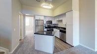 Located at 3765 S Emporia Way in Denver, Colorado, this two-story home offers a well-designed layout with notable architectural details throughout. The main living area immediately impresses with dramatic vaulted ceilings that stretch upward to the second floor, flooding the space with a sense of openness and volume. Large windows allow natural light to pour in, complementing the neutral carpet and soft wall tones. A built-in fireplace serves as a focal point in the living room, while an open upper-level loft overlooks the space below, fitted with track lighting.

The kitchen is outfitted with white cabinetry, dark granite-style countertops, a mosaic tile backsplash, and a full suite of stainless steel appliances including a refrigerator, range, microwave, and dishwasher. A central island provides additional prep and seating space, and wood-look flooring anchors the kitchen area.

Bedrooms are carpeted and receive natural light through windows with blinds, each equipped with a ceiling fan. Closet space is available with built-in hanging rods. The bathroom features a tub-shower combination with white tile and a dark accent border, paired with a vanity with dark countertops. A dedicated laundry room accommodates full-size washer and dryer units with overhead shelving.