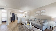 This single-floor residence offers a thoughtfully designed open-concept layout that seamlessly connects the living area to the kitchen. The living room is warm and inviting, featuring wood-style flooring, neutral-toned walls, and a textured ceiling. A large window allows generous natural light to fill the space, complementing the comfortable seating arrangement and glass-top coffee table.

The kitchen is a standout feature, boasting a striking two-tone design with crisp white upper cabinets and bold navy lower cabinets, all paired with light countertops and a classic subway tile backsplash. Stainless steel appliances, including a refrigerator, dishwasher, microwave, and range, complete this functional and stylish space. A pass-through opening connects the kitchen to the living area, enhancing the open feel.

The bedrooms are generously sized, each offering wood-style flooring, a bright window with blinds, and mirrored sliding closet doors with built-in shelving for ample storage. The primary bedroom connects directly to the main living area, creating an easy flow throughout the home.

Both bathrooms are finished with navy vanity cabinetry, light countertops, large framed mirrors, and a tub-shower combination with a curved curtain rod — clean, modern, and functional in design.