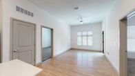 This single-floor unit showcases a clean, modern design throughout, with a thoughtful layout that balances open communal spaces and private rooms. The kitchen serves as a functional centerpiece, featuring white cabinetry with matte black hardware, a white subway tile backsplash, stainless steel appliances including a refrigerator, range, microwave, and dishwasher, and a white quartz center island that provides additional prep and seating space. Light wood-style flooring runs through the kitchen and living areas, contributing to a bright, cohesive aesthetic.

The living room is generously proportioned, with white walls, a ceiling fan, and a large window fitted with horizontal blinds that allows ample natural light while maintaining privacy. An adjacent carpeted room, visible through an open doorway, offers flexible use as a bedroom or secondary living space.

The bedrooms are carpeted for comfort, each featuring large windows with blinds that invite natural light and outdoor views. The primary bedroom connects to a bathroom and a walk-in closet equipped with wire shelving for organized storage.

The bathroom includes a full tub-shower combination, light wood-style flooring, a white vanity, and clean white walls, maintaining the unit's consistent, contemporary finish throughout.