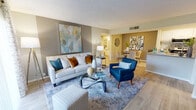 This single-floor residence offers a thoughtfully designed open-concept layout that seamlessly connects the living, dining, and kitchen areas. The living room is a welcoming space featuring light wood-style flooring, a textured ceiling, and neutral gray walls accented by bold artwork. A large sliding glass door floods the room with natural light and provides access to an outdoor area. The dining area, defined by warm gray tones and contemporary wall art, comfortably accommodates a round glass dining table with seating for several guests. The kitchen is equipped with stainless steel appliances, granite-style countertops, white cabinetry, and a convenient pantry closet, providing ample storage and workspace. The primary bedroom features natural light from a large window, light wood-style flooring, and a neutral color palette. The second bedroom is highlighted by a soft teal accent wall, artwork, and generous natural light, creating a calm and inviting retreat. The bathroom includes a full tub-shower combination with white tile surround, granite-topped vanity, and wood-style flooring. Throughout the residence, consistent light flooring, cohesive neutral tones, and modern finishes create a harmonious and contemporary ambiance.