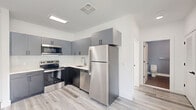 Located at 77 William St in Belleville, NJ, this well-appointed one-bedroom, one-bathroom unit offers a thoughtfully designed layout across a single floor. Light gray wood-style flooring runs throughout the space, lending a clean and cohesive aesthetic. The kitchen is a standout feature, outfitted with modern gray cabinetry, quartz countertops, a white subway tile backsplash, and a full suite of stainless steel appliances including a refrigerator, electric range, over-the-range microwave, and dishwasher — all finished to a contemporary standard. The bedroom is a bright, comfortable retreat with crisp white walls and a large window fitted with a navy roller shade, offering scenic views of the surrounding Belleville neighborhood and filling the room with natural light. A wall-mounted PTAC unit provides climate control. The bathroom is cleanly finished with large-format tile flooring, gray accent walls, a soaking tub, and a chrome towel bar, accessed through a paneled white door. The overall ambiance of the unit is modern, light-filled, and move-in ready, reflecting a fresh, minimalist design sensibility throughout.