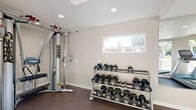 Located at 6413 Tupelo Dr in Citrus Heights, California, this dedicated exercise room is a compact yet efficiently designed fitness space that offers a comprehensive workout environment. The room features rubber flooring throughout, providing a durable and slip-resistant surface well-suited for exercise. Recessed lighting in the textured ceiling ensures bright, even illumination across the entire space.

Natural light flows in through multiple windows positioned along the walls, offering views of the surrounding greenery and creating an open, energizing atmosphere. A set of glass French doors on one end of the room provides direct access to an outdoor patio area, further enhancing ventilation and connectivity to the exterior.

A large wall-mounted mirror spans one side of the room, visually expanding the space and allowing users to monitor their form during workouts. The fitness equipment on hand is both varied and professional-grade, including Matrix brand treadmill and elliptical machines for cardiovascular training, a Hoist cable multi-gym for strength and resistance work, a tiered dumbbell rack stocked with hex weights, and an adjustable workout bench. The neutral, warm-toned walls and clean, minimalist design keep the focus on functionality, making this exercise room a practical and well-appointed space for fitness in the Citrus Heights community.