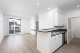 This single-floor unit features a clean, modern design with an open-concept layout connecting the kitchen and living areas. The kitchen is equipped with white cabinetry, dark granite-style countertops, stainless steel appliances including a refrigerator and dishwasher, and a peninsula that doubles as a breakfast bar. Recessed lighting illuminates the space throughout. Light wood-style flooring extends across the main living and kitchen areas, lending a warm, cohesive feel.

The living area is bright and open, with a sliding glass door leading to a private balcony that offers views of the surrounding neighborhood. The bedroom features plush carpeting, a ceiling fan, and a large window with vertical blinds, providing ample natural light and outdoor views. A closet with louvered doors adds practical storage.

The bathroom includes a white vanity with dark countertops, a tub-shower combination, and wood-style flooring that complements the rest of the unit. A laundry closet with additional storage is also present. The overall aesthetic is contemporary and functional, with a neutral color palette of whites and soft beiges throughout.
