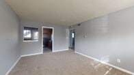 This single-floor residence at Cascades on the River offers a straightforward and functional layout connecting key living spaces. The living room is a generously sized area finished with neutral-toned carpet and grey walls, with natural light filtering in through windows. A textured ceiling runs throughout, and a baseboard heating system provides warmth. The space opens directly toward the kitchen, creating an accessible flow between rooms.

The kitchen is well-equipped, featuring warm-toned wooden cabinetry, dark countertops, and a full suite of black appliances including a range, dishwasher, and refrigerator. Wood-look flooring adds a practical, durable surface underfoot, and a door with a window leads to the exterior, bringing in additional natural light.

The bedroom is a comfortable, carpeted room with a window that allows natural light, a baseboard heater, and a closet with a rod for hanging storage. A second smaller carpeted room, also with a window and baseboard heater, provides additional flexible living space.

The bathroom includes a white vanity, toilet, and a tiled tub-shower combination with a window above, complemented by wood-look flooring. The overall palette of grey walls and white trim creates a clean, consistent look throughout the unit.