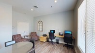 This single-floor business center offers a clean, functional workspace designed to meet everyday professional needs. The room features dual computer workstations arranged along a natural wood-toned desk running the length of one wall, each equipped with a desktop computer and ergonomic office chair. A printer and paper organizer are conveniently positioned between the two stations, ensuring shared resources are easily accessible.

The space is finished with wood-look flooring that adds warmth to the otherwise neutral palette of soft gray walls. Recessed lighting illuminates the room evenly, complementing the natural light. A decorative arched mirror mounted on the wall adds a subtle design element, enhancing the sense of openness.

A casual seating area near the entrance includes a patterned armchair and side table, providing a comfortable spot for informal meetings or waiting. A round table with dark chairs is also partially visible, offering an additional surface for collaborative work or review. The overall ambiance is calm and approachable, balancing practicality with a welcoming aesthetic suited for focused work.