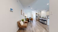 This two-story home offers a well-designed layout across two floors, providing ample space for comfortable living. The main floor features an open-concept kitchen, dining, and living area unified by light wood-style flooring throughout. The kitchen is equipped with stainless steel appliances, light wood cabinetry, dark granite countertops, and a breakfast bar with seating — ideal for both casual meals and entertaining. The living area flows naturally from the kitchen and dining space, featuring recessed lighting and a ceiling fan that enhances the bright, airy atmosphere created by large windows with plantation shutters. The upper floor hosts the four bedrooms, including a generously sized primary bedroom with its own en-suite bathroom featuring a dual-sink vanity with modern cabinetry, a large mirror, and a bright window. Additional bedrooms are well-proportioned with natural light and share access to the remaining bathrooms. A dedicated laundry room with full-size washer and dryer adds everyday convenience, while a spacious walk-in closet provides abundant storage. With five bathrooms across both floors, clean white walls, and consistent wood-style flooring, the home maintains a cohesive, contemporary aesthetic throughout.