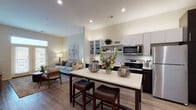 This single-floor residence features a thoughtfully designed open-concept layout where the kitchen, dining, and living areas flow seamlessly together. The kitchen is equipped with stainless steel appliances, including a refrigerator, range, and microwave, complemented by two-tone cabinetry in white and dark espresso finishes, open shelving, and a central island with bar seating — ideal for casual dining and entertaining. Wood-look flooring extends throughout the main living area, adding warmth and continuity.

The living room offers a comfortable, well-lit space anchored by French doors with transom windows that invite natural light and provide outdoor access. The bedroom features plush carpeting, a ceiling fan, and windows with views to the exterior, creating a calm and restful retreat. The full bathroom is finished with large-format tile flooring, a dark vanity with an extended countertop, and a tub-shower combination framed by classic subway tile.

A dedicated laundry room includes a full-size washer and dryer, upper cabinetry, and a folding counter — a practical and convenient feature. Recessed lighting throughout and a neutral color palette give the space a clean, modern ambiance suitable for a variety of lifestyles.
