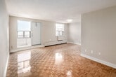 This one-bedroom, one-bathroom unit at 20 Paisley Blvd W in Mississauga offers a well-organized layout across a single floor. The living room is notably spacious for the unit's overall footprint, featuring gleaming parquet wood flooring that extends throughout the space. Two windows allow generous natural light to fill the room, with one accompanied by a balcony door that provides outdoor access and views of the surrounding area. Baseboard heating units run along the exterior walls, ensuring warmth throughout the space.

The bedroom is a comfortable size, also finished with the same warm parquet flooring. A large window frames an open skyline view, and a built-in closet with bi-fold doors provides practical storage. The kitchen is efficiently designed with grey cabinetry, granite-style countertops, light tile flooring, and a white electric range, with an adjacent pass-through connecting it to the main living areas.

The bathroom features a clean, classic design with a full-sized soaker tub and shower combination, finished with white subway tiles and chrome fixtures. Neutral grey walls and white trim are consistent throughout the unit, lending a clean, cohesive aesthetic. The overall ambiance is bright, functional, and well-maintained.