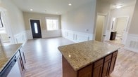 This well-appointed single-story, 2-bedroom, 2-bathroom home offers a thoughtfully designed open-concept floor plan that maximizes both space and functionality. The main living area seamlessly connects to the kitchen, creating an inviting atmosphere ideal for everyday living and entertaining. The kitchen features warm, rich cabinetry topped with stunning granite countertops, including a large island that serves as a natural gathering point and provides ample prep space. Light wood-tone flooring flows throughout the main living areas, adding warmth and continuity to the design. The living and dining area is distinguished by elegant raised-panel wainscoting along the lower walls, lending a classic architectural detail that elevates the overall aesthetic. Recessed lighting in the ceiling provides clean, modern illumination, while a front-facing window and decorative front door with sidelight allow natural light to fill the space. The neutral wall tones throughout create a bright, versatile backdrop that complements a variety of décor styles. With its combination of classic detailing and contemporary finishes, this home offers a comfortable and stylish living environment across its single, well-organized floor.