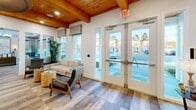 This 910 square foot space in Gainesville, FL, showcases a harmonious blend of modern and rustic design. The single-floor layout boasts an open concept, maximizing the use of space. Exposed wooden beam ceilings add warmth and character, while large windows flood the interior with natural light, creating an airy atmosphere.

The space is versatile, featuring distinct areas for various functions. A cozy seating area near the entrance provides a welcoming environment, complemented by stylish mid-century modern furniture. The kitchenette, adorned with blue cabinetry and stainless steel appliances, offers a pop of color against the white walls.

Throughout the space, hardwood flooring ties the rooms together, enhancing the overall aesthetic. Multiple seating arrangements, including a round table with unique woven chairs, cater to different needs - from casual meetings to relaxation. Modern amenities such as a wall-mounted TV and computer workstation are seamlessly integrated.

The decor is a thoughtful mix of contemporary and natural elements, with potted plants, abstract art, and carefully chosen accessories adding visual interest. The abundance of windows not only brightens the space but also provides views of the surrounding area, connecting the interior to its exterior environment.

This multifunctional space effectively combines work and leisure areas, making it suitable for a variety of uses while maintaining a cohesive and inviting atmosphere.