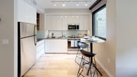 Located in the vibrant U Street corridor of Washington, DC, this contemporary single-floor residence offers a thoughtfully designed open-concept layout. The living area is bright and welcoming, anchored by large floor-to-ceiling sliding glass doors that open onto a private balcony, allowing abundant natural light and views of the landscaped courtyard below. Light hardwood flooring flows seamlessly throughout the main living spaces, reinforcing a clean, modern aesthetic.

The kitchen is efficiently appointed with sleek white cabinetry, stainless steel appliances including a full-size refrigerator, microwave, and range, complemented by a light subway tile backsplash and track lighting overhead. A compact bar-height bistro table with modern stools provides an intimate dining option adjacent to the kitchen window.

The bedroom features neutral tones, warm carpeting, and a sliding double-door closet offering ample storage. The full bathroom is finished with large-format gray tile flooring, classic white subway tile surrounding the soaking tub and shower combination, and a modern vanity with a wood-toned cabinet and white countertop.

The private balcony overlooks a well-maintained communal courtyard with greenery and seating areas, providing a pleasant outdoor retreat. The building's contemporary brick and glass exterior architecture completes this well-appointed urban residence.