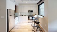 Located in the vibrant U Street corridor of Washington, DC, this contemporary single-floor residence offers a thoughtfully designed open-concept layout. The living area is bright and welcoming, anchored by large floor-to-ceiling sliding glass doors that open onto a private balcony, allowing abundant natural light and views of the landscaped courtyard below. Light hardwood flooring flows seamlessly throughout the main living spaces, reinforcing a clean, modern aesthetic.

The kitchen is efficiently appointed with sleek white cabinetry, stainless steel appliances including a full-size refrigerator, microwave, and range, complemented by a light subway tile backsplash and track lighting overhead. A compact bar-height bistro table with modern stools provides an intimate dining option adjacent to the kitchen window.

The bedroom features neutral tones, warm carpeting, and a sliding double-door closet offering ample storage. The full bathroom is finished with large-format gray tile flooring, classic white subway tile surrounding the soaking tub and shower combination, and a modern vanity with a wood-toned cabinet and white countertop.

The private balcony overlooks a well-maintained communal courtyard with greenery and seating areas, providing a pleasant outdoor retreat. The building's contemporary brick and glass exterior architecture completes this well-appointed urban residence.
