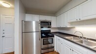 Located at 1105 NC-54 Hwy Byp in Chapel Hill, NC, this single-floor residence offers a practical and comfortable layout with consistent hardwood-style flooring throughout the living areas and bedrooms. The kitchen is equipped with stainless steel appliances, including a full-size refrigerator, electric range with oven, and over-the-range microwave. White raised-panel cabinetry provides ample storage, while dark countertops and a stainless steel sink complete the functional workspace. A pass-through opening connects the kitchen to the living area, creating an open and communicative flow between the two spaces. The living area is generously sized, featuring a textured ceiling and neutral wall tones that contribute to a clean, versatile aesthetic. Bedrooms are well-proportioned, with one room offering two windows that allow natural light to fill the space, along with a ceiling fan fixture. Another bedroom includes a standard closet with a hanging rod, providing convenient storage. The bathroom features a full-size soaking tub with a clean, bright surround. Throughout the unit, white trim and neutral gray walls maintain a cohesive, move-in-ready appearance suited for a variety of furnishing styles.
