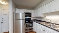 Located at 1105 NC-54 Hwy Byp in Chapel Hill, NC, this single-floor residence offers a practical and comfortable layout with consistent hardwood-style flooring throughout the living areas and bedrooms. The kitchen is equipped with stainless steel appliances, including a full-size refrigerator, electric range with oven, and over-the-range microwave. White raised-panel cabinetry provides ample storage, while dark countertops and a stainless steel sink complete the functional workspace. A pass-through opening connects the kitchen to the living area, creating an open and communicative flow between the two spaces. The living area is generously sized, featuring a textured ceiling and neutral wall tones that contribute to a clean, versatile aesthetic. Bedrooms are well-proportioned, with one room offering two windows that allow natural light to fill the space, along with a ceiling fan fixture. Another bedroom includes a standard closet with a hanging rod, providing convenient storage. The bathroom features a full-size soaking tub with a clean, bright surround. Throughout the unit, white trim and neutral gray walls maintain a cohesive, move-in-ready appearance suited for a variety of furnishing styles.