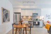 Located at 205 Queen St E in Brampton, Ontario, this thoughtfully designed one-bedroom, one-bathroom unit offers a clean, modern aesthetic with light-toned hardwood-style flooring and crisp white walls throughout. The open-concept layout connects the kitchen and living area seamlessly, maximizing the efficient use of space. The kitchen is outfitted with white flat-panel cabinetry extending to the ceiling, a grey tile backsplash, stainless steel appliances including a full-size refrigerator, and a double sink — all complemented by a dining area with room for a full table. The bright living room benefits from large sliding glass doors that open to a private balcony, flooding the space with natural light and offering open views of the surrounding Brampton cityscape. The bedroom continues the light-filled theme with its own floor-to-ceiling sliding door balcony access, roller blinds, and a dedicated walk-in closet. The bathroom features a clean, neutral palette with a vanity, framed mirror, and a stacked in-unit washer and dryer tucked neatly beside it. Throughout the unit, recessed lighting and modern fixtures contribute to the space's polished, contemporary ambiance.