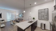 Located at 3320 N Seventh Ave in Phoenix, AZ, this single-story residence showcases a contemporary design with clean lines, crisp white walls, and wood-style flooring throughout. The open-concept layout seamlessly connects the living area to the kitchen, creating a cohesive and functional living space. The living room features a sliding glass door that invites natural light and provides outdoor access, complemented by high ceilings that enhance the sense of spaciousness.

The kitchen is a standout feature, centered around a large island with striking granite countertops, an undermount double sink, and a high-arc faucet. Dark cabinetry pairs elegantly with stainless steel appliances, including a refrigerator, microwave, and gas range, while pendant lighting above the island adds a refined touch. Bar-height seating along the island offers a casual dining option.

The bedroom benefits from soaring vaulted ceilings and a ceiling fan, contributing to an airy atmosphere. The bathroom continues the home's design language with granite countertops, dark vanity cabinetry, a framed mirror, and a glass-enclosed walk-in shower with tile surround. The consistent use of quality finishes throughout unifies the space with a polished, modern aesthetic.