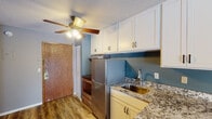 Located at 3621 Lancaster Ln N in Plymouth, Minnesota, this single-floor unit offers a functional, open-concept layout connecting the kitchen and living areas. The kitchen is outfitted with white shaker-style cabinetry providing ample storage, granite countertops, a stainless steel refrigerator, and a stainless steel range. A peninsula with bar seating and an integrated sink separates the kitchen from the adjoining living space, creating a natural flow between the two areas. A ceiling fan overhead adds comfort and airflow throughout. The living area is finished with wood-look vinyl plank flooring and painted in a calming combination of muted blue and gray tones. A sliding glass door draws in natural light and opens to a private deck with outdoor views. Baseboard heating runs along the walls, and a textured ceiling is consistent throughout the unit. The bedroom features the same durable flooring and neutral gray walls, with baseboard heating and a clean, open feel. The bathroom includes a full tub and shower combination with a white tile surround and oil-rubbed bronze fixtures. Overall, the space presents a cohesive, updated aesthetic suited for comfortable everyday living.