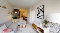 This well-appointed single-floor residence showcases a clean, contemporary design with a cohesive neutral palette and light wood-style flooring throughout. The open-concept living area flows seamlessly from the living room to the dining space and kitchen, creating an inviting and functional layout. The living room features crisp white walls, ample natural light, and modern décor accents that enhance the bright, airy ambiance.

The kitchen is thoughtfully designed with two-tone cabinetry — dark lower cabinets paired with glossy white uppers — complemented by white quartz countertops, a chevron-pattern tile backsplash, and a full suite of stainless steel Whirlpool appliances including a range, over-the-range microwave, and dishwasher.

The primary bedroom is a standout, featuring floor-to-ceiling windows that frame impressive urban skyline views and flood the room with natural light. The second bedroom is comfortably sized with built-in closet storage and a soft, neutral finish. Both rooms offer a calm, restful atmosphere.

Two bathrooms serve the residence. The primary bath includes a dark wood floating vanity with a white countertop and a glass-enclosed walk-in shower with tile surround. The second bathroom features a soaking tub and shower combination with large-format light tile and polished chrome fixtures, completing this refined and functional urban home.