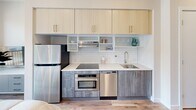 Located in Philadelphia's Spring Garden neighborhood, this thoughtfully designed one-bedroom, one-bathroom residence maximizes every inch of its compact footprint across a single floor. The modern kitchen anchors one end of the unit, outfitted with stainless steel appliances including a refrigerator, wall oven, dishwasher, and induction cooktop. White subway tile backsplash, light wood upper cabinetry, and gray lower cabinets create a clean, contemporary aesthetic with ample storage. The bedroom is a masterclass in smart design, featuring a built-in Murphy bed system flanked by floor-to-ceiling cabinetry in light wood tones. An integrated desk nook provides a dedicated workspace, while a small dining area with a round table and seating offers a functional living zone. Warm hardwood flooring runs throughout, contributing to the cohesive, airy feel of the space. The bathroom is finished in light neutral tones with large-format floor tiles, a wall-mounted toilet, modern vanity with under-cabinet storage, a backlit mirror, and a shower-tub combination. Clean white walls and recessed lighting throughout the unit enhance the sense of brightness and openness, making this a highly functional and well-appointed residence.