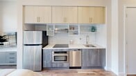 Located in Philadelphia's Spring Garden neighborhood, this thoughtfully designed one-bedroom, one-bathroom residence maximizes every inch of its compact footprint across a single floor. The modern kitchen anchors one end of the unit, outfitted with stainless steel appliances including a refrigerator, wall oven, dishwasher, and induction cooktop. White subway tile backsplash, light wood upper cabinetry, and gray lower cabinets create a clean, contemporary aesthetic with ample storage. The bedroom is a masterclass in smart design, featuring a built-in Murphy bed system flanked by floor-to-ceiling cabinetry in light wood tones. An integrated desk nook provides a dedicated workspace, while a small dining area with a round table and seating offers a functional living zone. Warm hardwood flooring runs throughout, contributing to the cohesive, airy feel of the space. The bathroom is finished in light neutral tones with large-format floor tiles, a wall-mounted toilet, modern vanity with under-cabinet storage, a backlit mirror, and a shower-tub combination. Clean white walls and recessed lighting throughout the unit enhance the sense of brightness and openness, making this a highly functional and well-appointed residence.