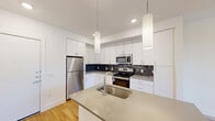 Located at 6306 McNeil Dr in Austin, TX, this well-designed one-bedroom, one-bathroom unit offers a clean, modern aesthetic across a single floor. The open-concept layout connects the kitchen and living area seamlessly, creating an efficient and inviting flow. The kitchen is a standout feature, equipped with stainless steel appliances including a refrigerator, range, and microwave, complemented by sleek white cabinetry, a dark tile backsplash, and a central island with a quartz countertop and undermount sink. Stylish pendant lighting illuminates the kitchen and living area, where a ceiling fan adds practical comfort. Warm hardwood-style flooring extends throughout the entire unit, lending a cohesive and contemporary feel. A hallway leads to the private bedroom, which features a window with exterior views and ample natural light. The dedicated closet provides organized storage nearby. The bathroom is finished with white subway tile surrounding the tub-shower combination, a floating white vanity, recessed lighting, and matching hardwood-style flooring, maintaining the unit's consistent modern palette. The crisp white walls throughout enhance the sense of brightness and space, making this a functional and stylish residence in Austin.
