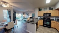 This single-floor residence offers a thoughtfully designed open-concept layout that seamlessly connects the kitchen, dining, and living areas. The kitchen is equipped with warm maple cabinetry, dark granite-style countertops, black appliances, and a central island with a built-in sink — ideal for both cooking and casual entertaining. A skylight above the kitchen adds to the bright, welcoming atmosphere.

The living room features wood-style flooring, neutral walls, and large sliding glass doors that open to an outdoor balcony, flooding the space with natural light and providing pleasant outdoor views. The adjacent dining area is distinguished by a bold teal accent wall, ceiling fan, and ample natural light from a side window, creating an intimate yet airy setting.

The primary bedroom is a standout, showcasing a vibrant teal accent wall, plush carpeting, ceiling fan, and large windows dressed with layered curtains for privacy and light control. A second bedroom offers a tray ceiling detail, ceiling fan, and generous natural light. The full bathroom features an extended vanity with wood cabinetry, a wide mirror, and wood-style flooring, with an adjacent built-in desk nook providing a functional workspace. Throughout the residence, a cohesive teal and neutral color palette lends a modern, polished aesthetic.