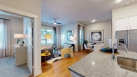 This single-story residence is thoughtfully designed with an open-concept floor plan that seamlessly connects the kitchen, dining, and living areas. The kitchen serves as a central hub, featuring white shaker cabinetry extending to the ceiling, granite countertops, a subway tile backsplash, stainless steel appliances, and a peninsula island with bar seating—ideal for casual dining or entertaining. Hardwood-style flooring flows throughout the main living areas, complementing the bright, neutral palette.

The living room offers generous natural light through multiple windows dressed with blinds and floor-length curtains, and is topped with a ceiling fan for added comfort. A dedicated dining area sits adjacent, completing the cohesive social space.

The primary bedroom features plush carpeting and direct access to a spacious walk-in closet with built-in shelving. Its en suite bathroom includes a granite-topped double vanity with white cabinetry and ample storage. A secondary bedroom and an additional full bathroom with a tub-shower combination and white tile surround provide comfortable accommodations for guests. Throughout, the space maintains a clean, modern aesthetic with consistent finishes.