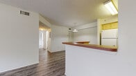 Located at 120 Carolina Lake Dr in Daytona Beach, Florida, this 2-bedroom, 1-bathroom residence offers a functional and well-laid-out single-floor plan. The open-concept kitchen and living area forms the heart of the home, where wood-style laminate flooring flows seamlessly throughout. The kitchen is equipped with light wood cabinetry, a full suite of white appliances including a refrigerator and electric range, a built-in range hood, and a breakfast bar with a warm-toned countertop that separates the kitchen from the living area. A pendant light fixture adds a subtle decorative touch overhead, complemented by a textured ceiling. The primary bedroom is generously sized, featuring plush carpeting, a ceiling fan, and a large window dressed with vertical blinds that allows ample natural light. It is accompanied by a dedicated walk-in closet with wire shelving for organized storage. The second bedroom also offers wood-style flooring and a wide window with views of surrounding greenery. Both bedrooms include built-in closets with louvered bifold doors. The full bathroom features a tiled tub-shower combination, wood-look flooring, and light wood vanity cabinetry. A hallway connects all rooms, providing a clear and convenient flow throughout the residence.